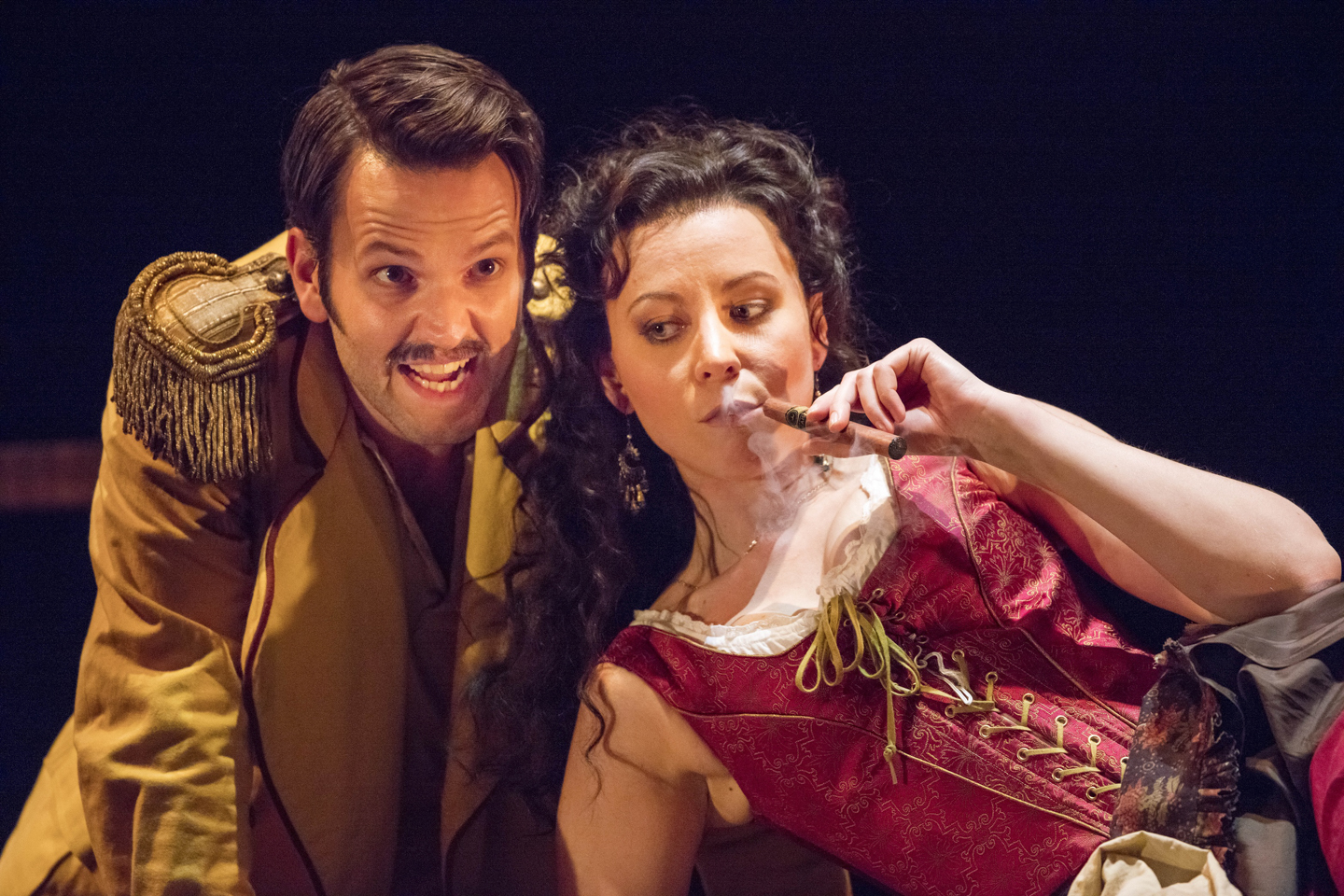 Timothy Dickinson as Zuniga leaning beside Justina Gringyte as Carmen, who is smoking a cigar, in Carmen