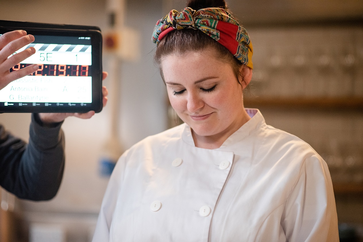 Soprano Charlie Drummond (Belle) wearing a white chef jacket and colourful bandanna during filming of The Narcissistic Fish